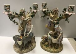 A pair of Continental biscuit fired porcelain and glazed figural candlesticks as fruit pickers,