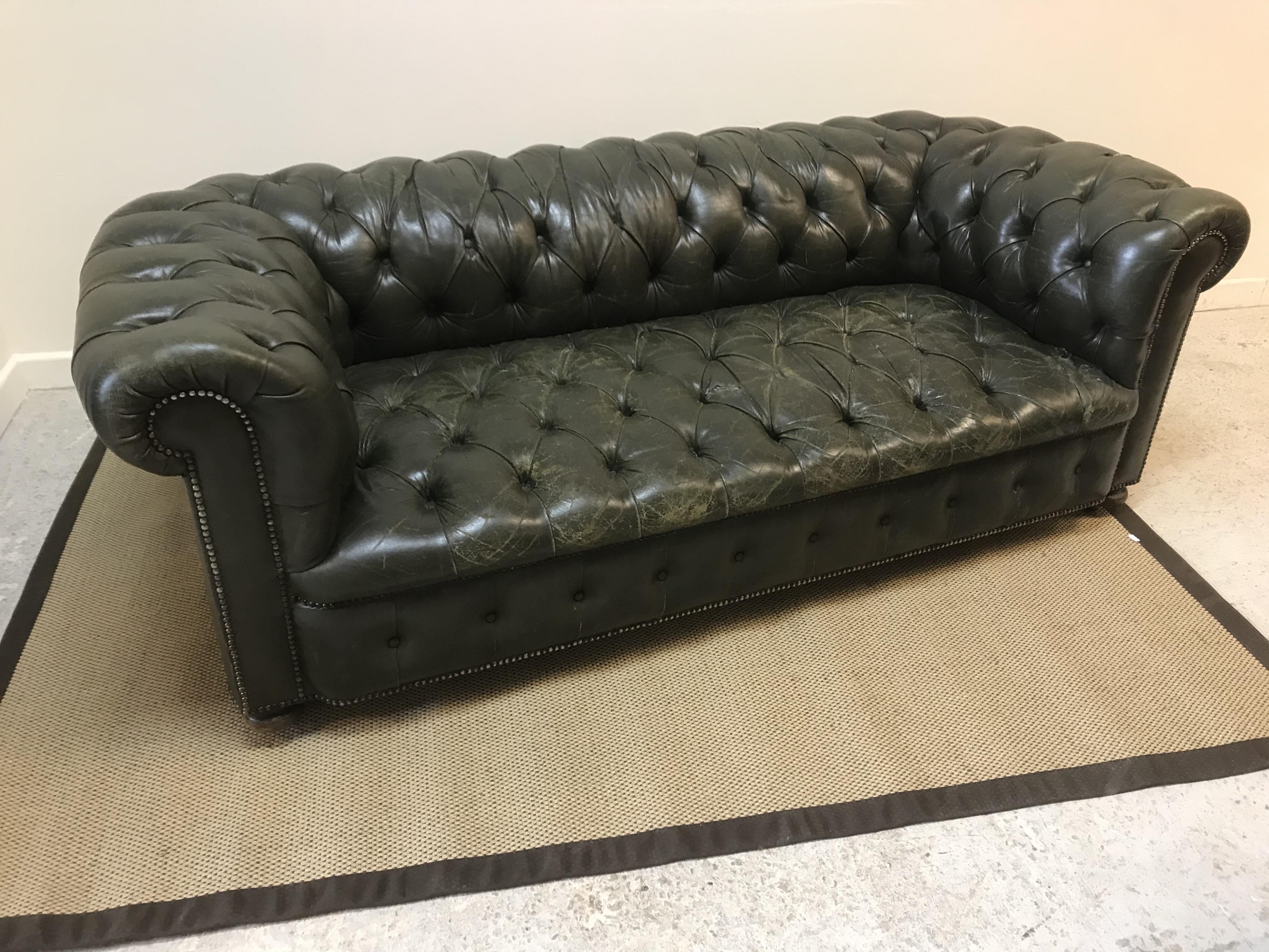 An early 20th Century green buttoned leather upholstered scroll arm Chesterfield sofa on squat bun