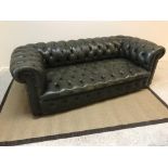 An early 20th Century green buttoned leather upholstered scroll arm Chesterfield sofa on squat bun