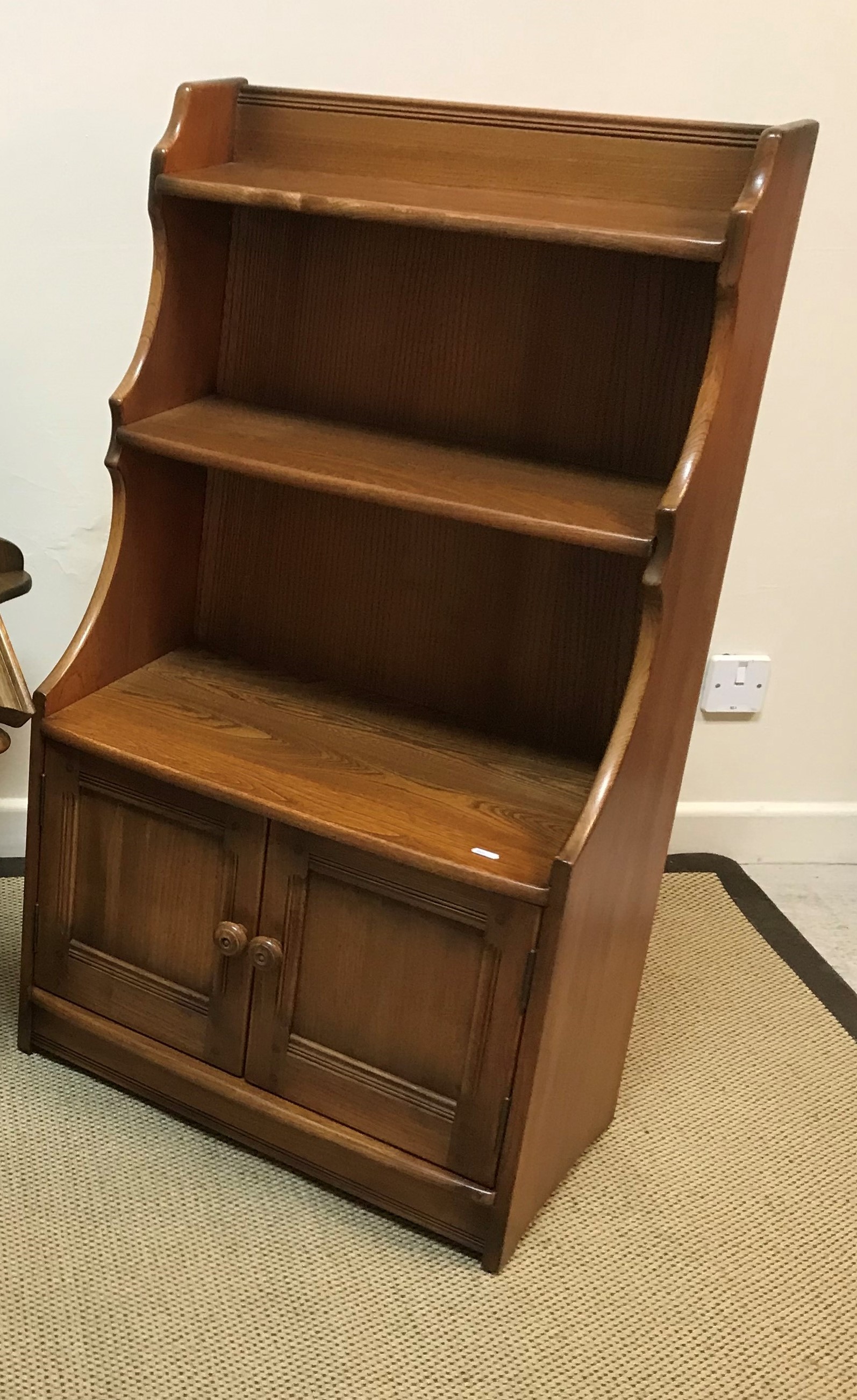 An Ercol elm side cabinet with two open shelves over two panelled cupboard doors, 61 cm wide x 33.