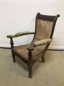 A 19th Century teak and caned plantation type chair with reeded scroll back rail and upholstered