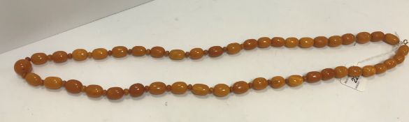 An amber bead necklace with central spherical bead flanked by 45 graduated ovoid beads,