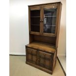 An Ercol elm side cabinet with two glazed cabinet doors enclosing two shelves over a recess,