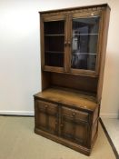 An Ercol elm side cabinet with two glazed cabinet doors enclosing two shelves over a recess,