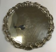 A late Victorian silver salver with piecrust and shell decorated rim, raised on three scroll feet,