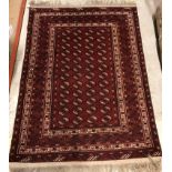 A Bokhara rug, the central panel set with elephant foot medallions on a dark red ground,