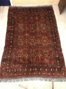 A Persian rug, the central panel set with repeating motifs on a blood red ground,