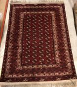 A Bokhara rug, the central panel set with elephant foot medallions on a dark red ground,