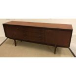 A 1960's teak sideboard with three central drawers flanked by two cupboard doors on elliptical