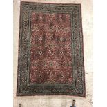 A Persian rug, the central panel set with all-over floral decoration on a pink ground, within a