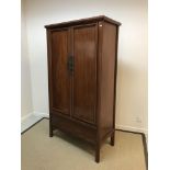 A 20th Century Chinese cherry wood two door wardrobe of tapering form, raised on plain rounded