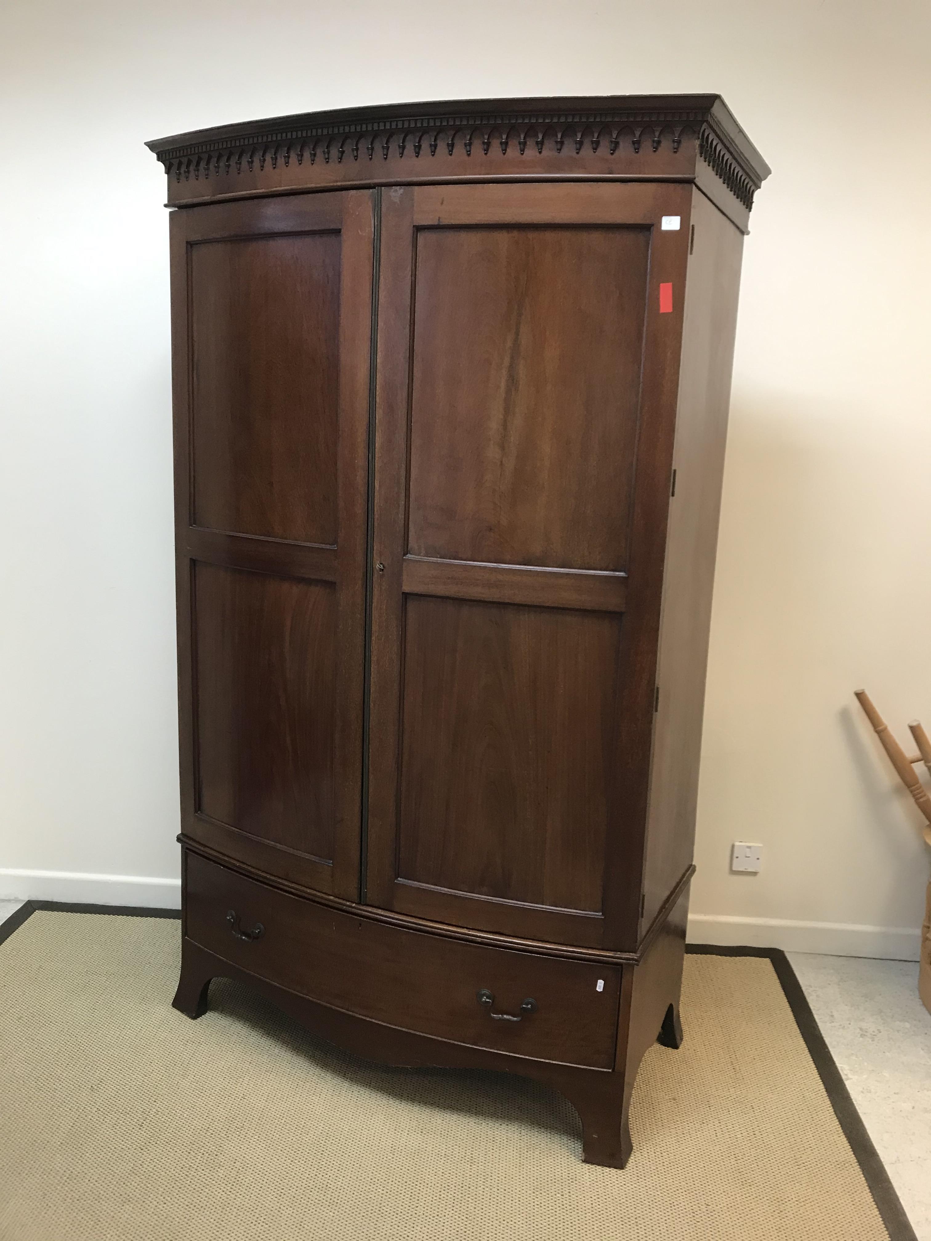 An Edwardian mahogany bow fronted wardrobe, the moulded dentil cornice over two twin-panelled