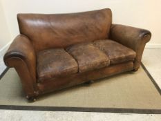An early 20th Century mid brown leather upholstered scroll arm sofa, on squat bun feet to castors (