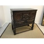 An oak cupboard on stand in the 17th Century manner, the upper section with two panelled cupboard