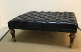 A large buttoned leather topped ottoman, raised on Victorian carved oak legs to brass caps and