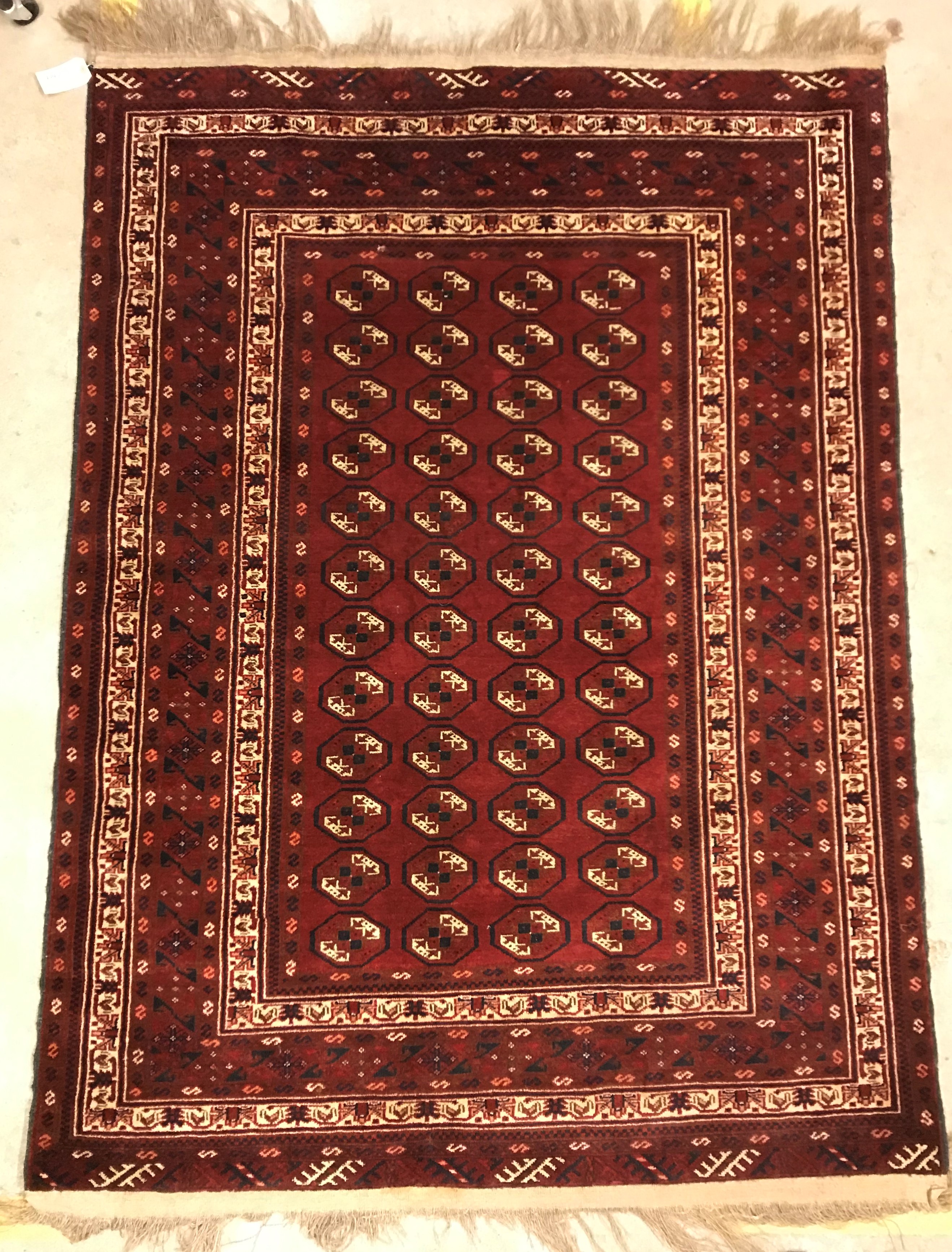 A Bokhara rug, the central panel set with repeating elephant foot style medallions on a dark red