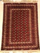A Bokhara rug, the central panel set with repeating elephant foot style medallions on a dark red