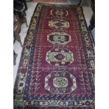 A Persian rug with five repeating elephant foot medallions on a purple ground within a stepped