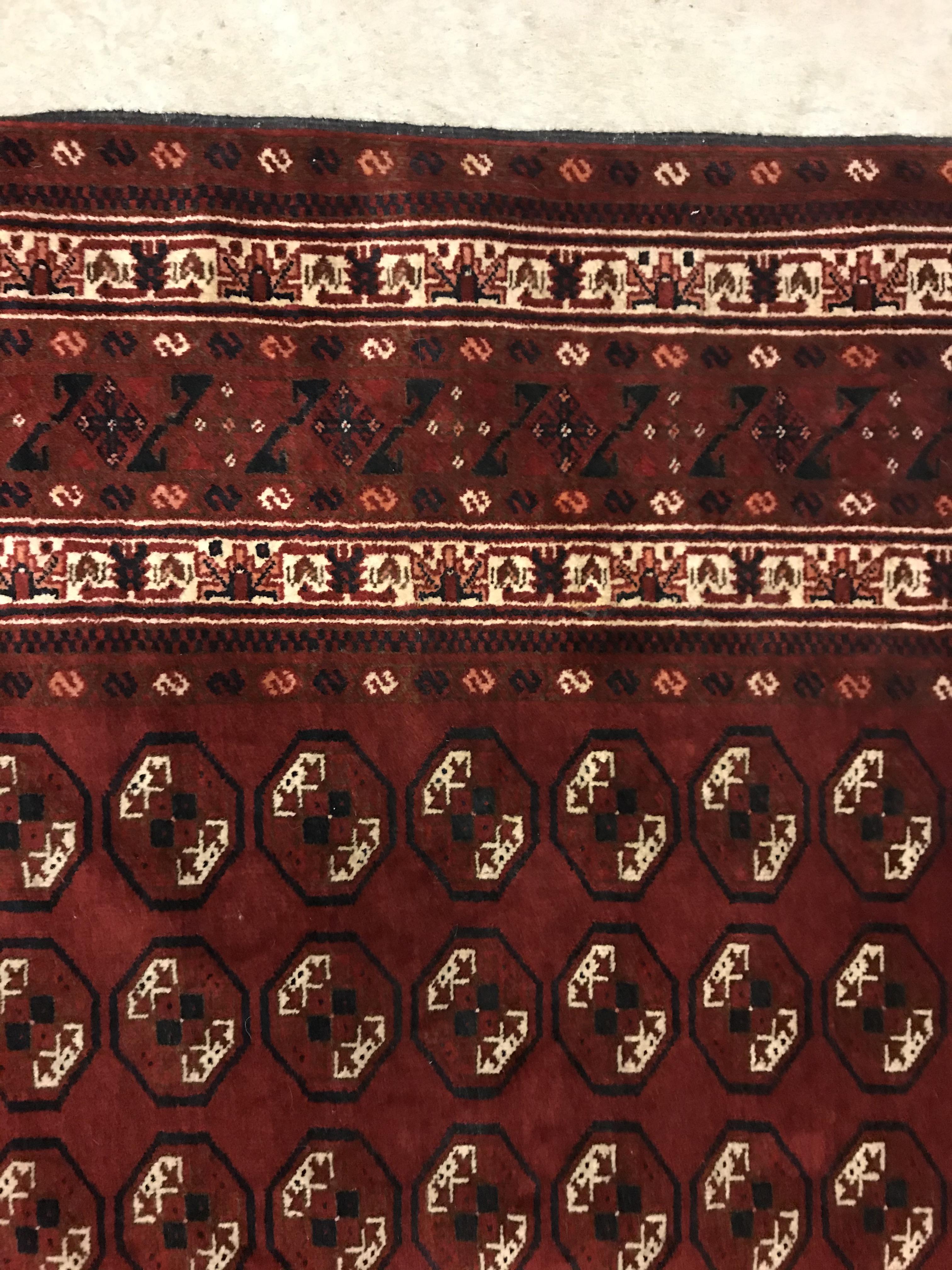 A Bokhara rug, the central panel set with repeating elephant foot style medallions on a dark red - Image 6 of 12
