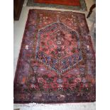 A Persian rug, the central panel set with a lozenge shaped medallion on a red floral decorated