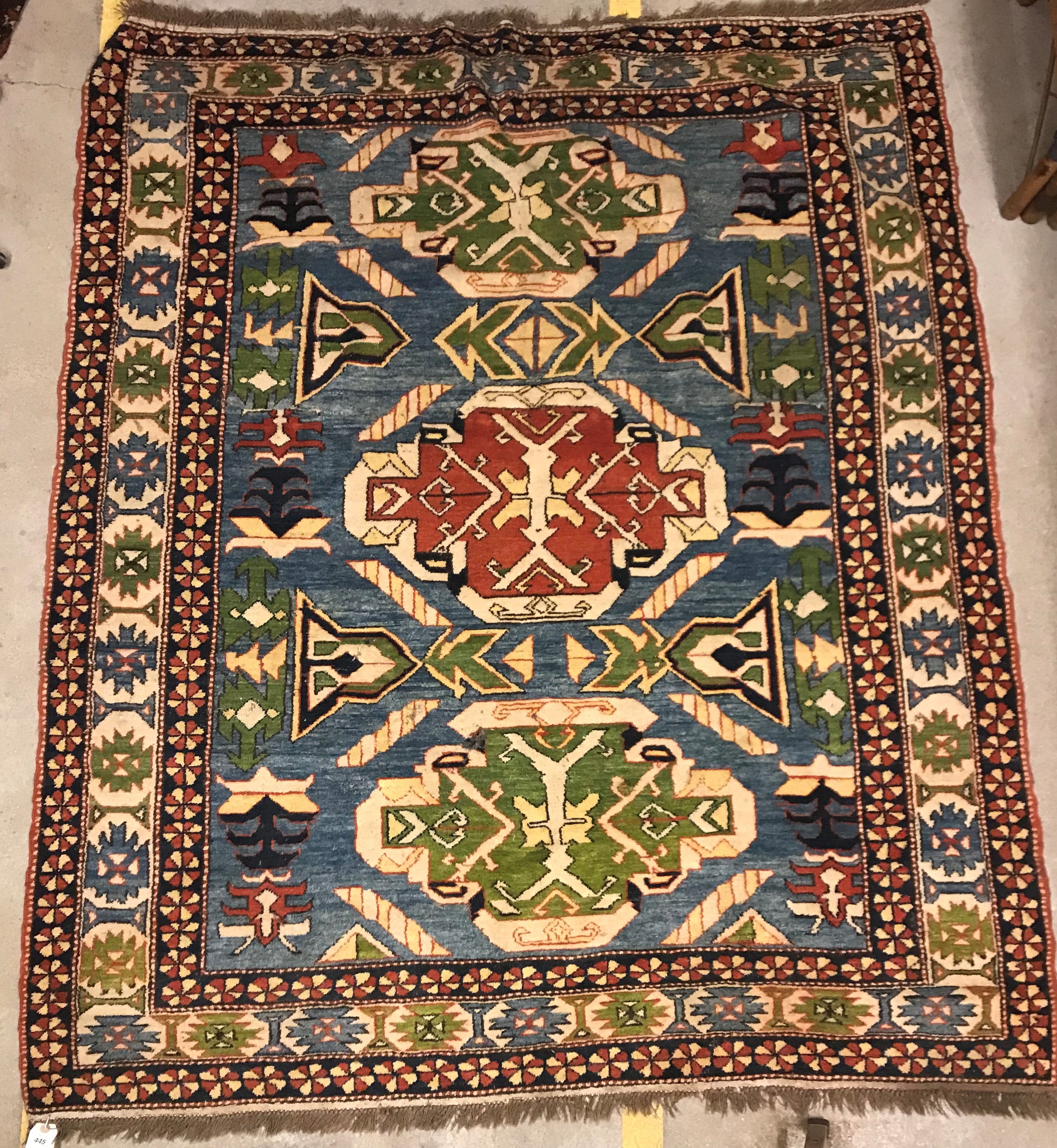 A Caucasian rug, the central panel set with three repeating medallions on a pale blue ground, within