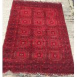A Bokhara rug with repeating medallions on a red ground, within a red and black stepped geometric