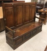 A 19th Century oak hall settle, the four fielded panelled back over a box seat, flanked by open arms