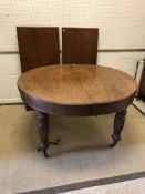 A Victorian oak dining table, the circular top raised on ringed and turned legs to brass caps and