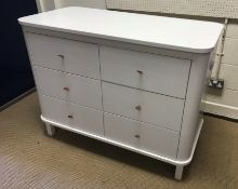 A modern white painted MDF chest of six drawers with brown leather loop handles, flanked by pull-out