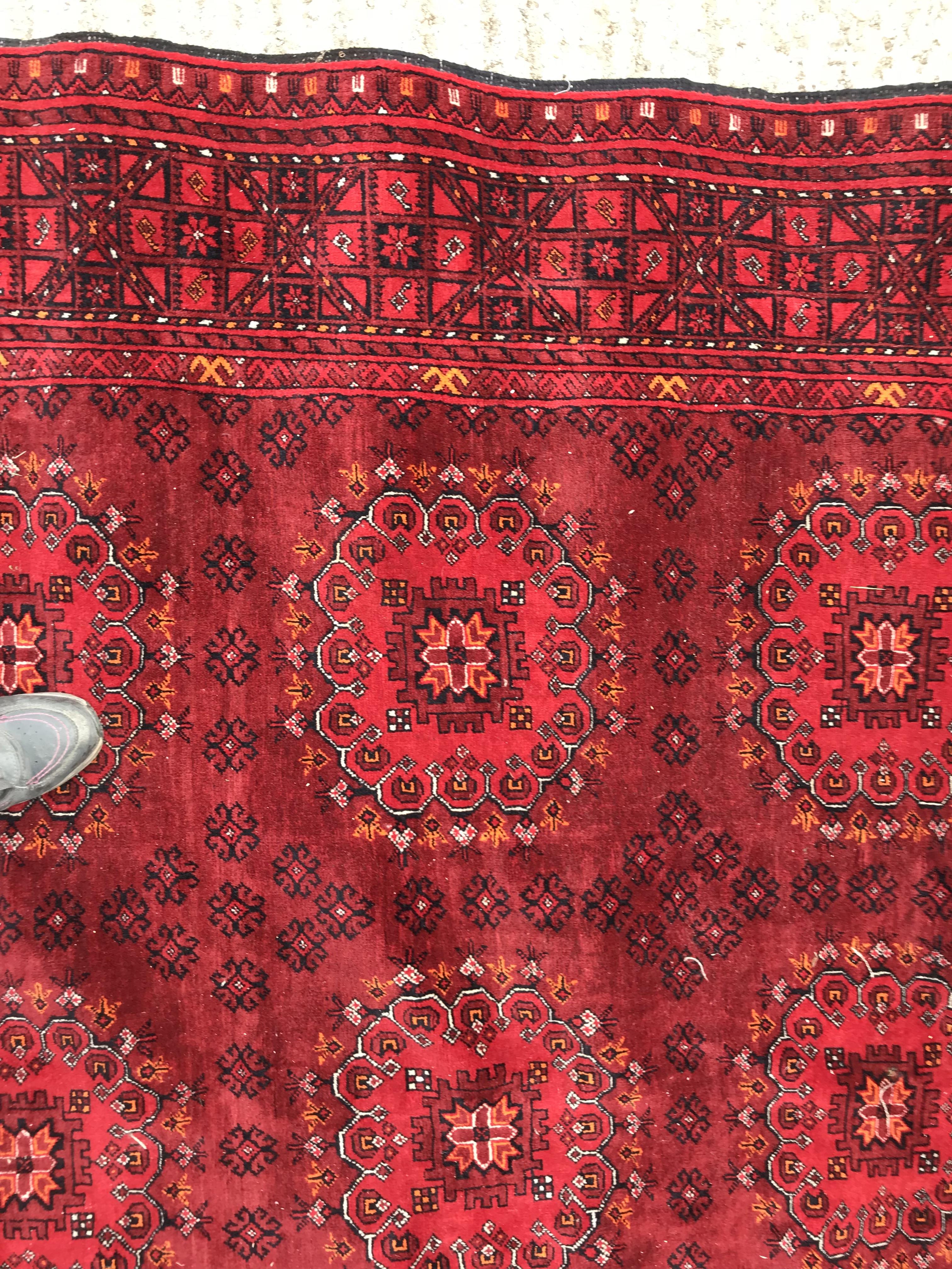 A Bokhara rug with repeating medallions on a red ground, within a red and black stepped geometric - Image 2 of 4