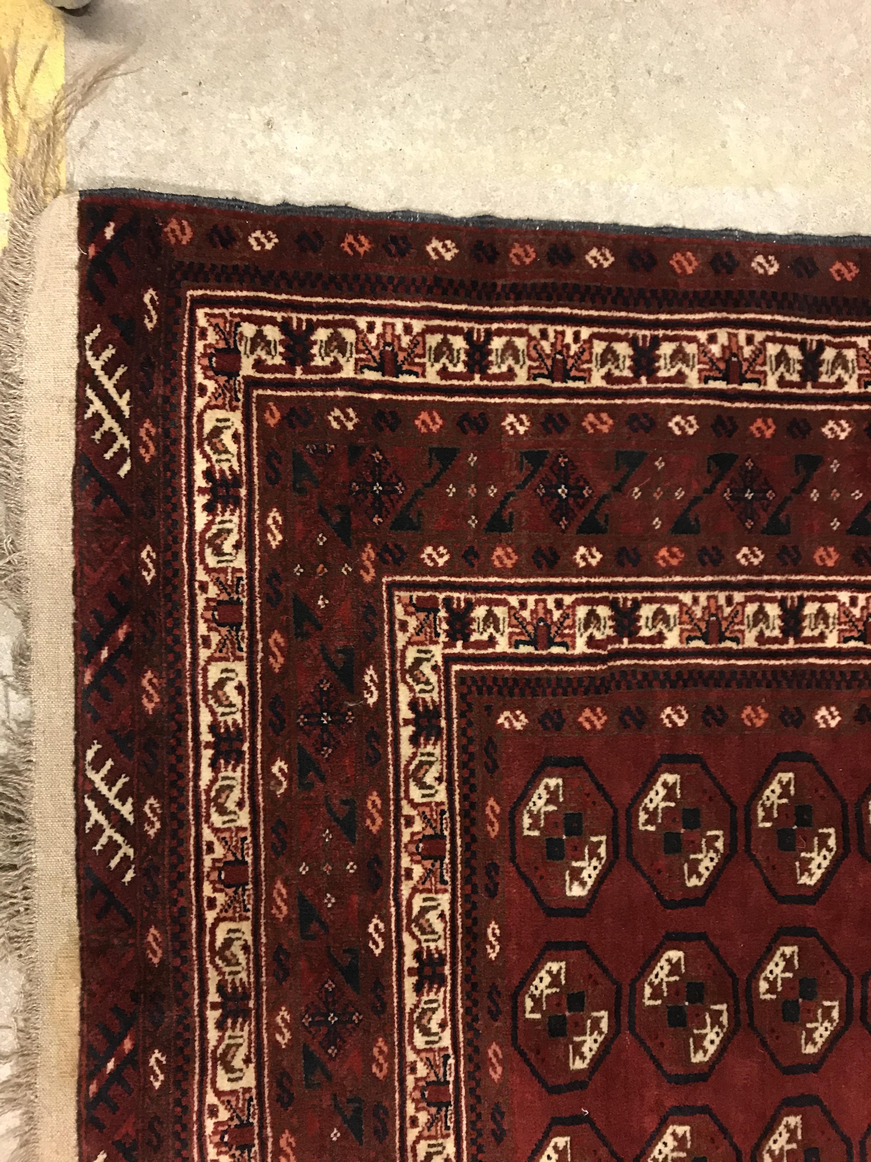 A Bokhara rug, the central panel set with repeating elephant foot style medallions on a dark red - Image 2 of 12