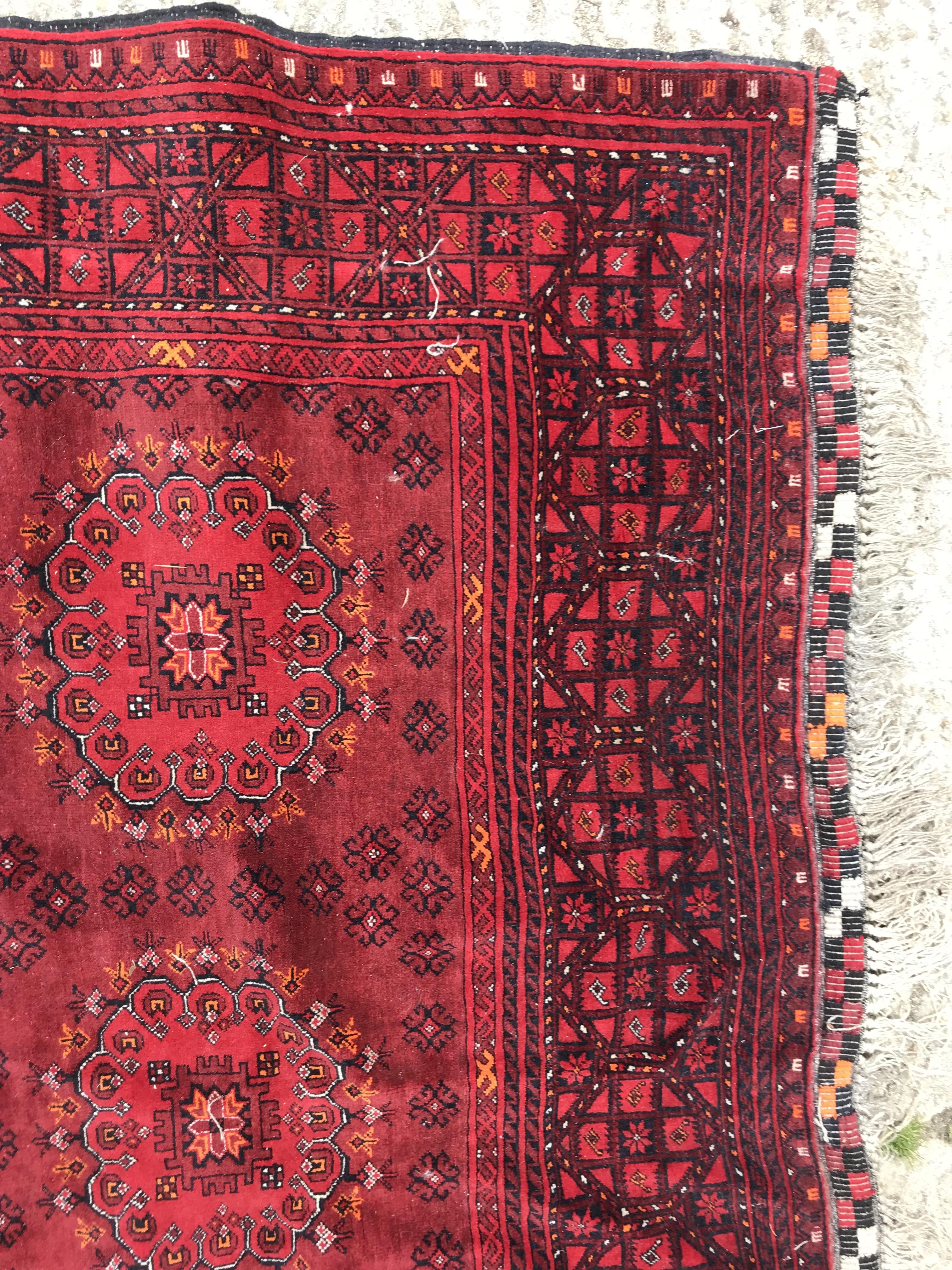 A Bokhara rug with repeating medallions on a red ground, within a red and black stepped geometric - Image 3 of 4