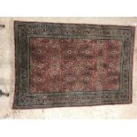 A Persian rug, the central panel set with all-over floral decoration on a pink ground, within a