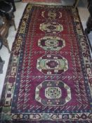 A Persian rug with five repeating elephant foot medallions on a purple ground within a stepped