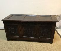 An 18th Century oak coffer, the plain three panel top over a foliate carved frieze and three foliate