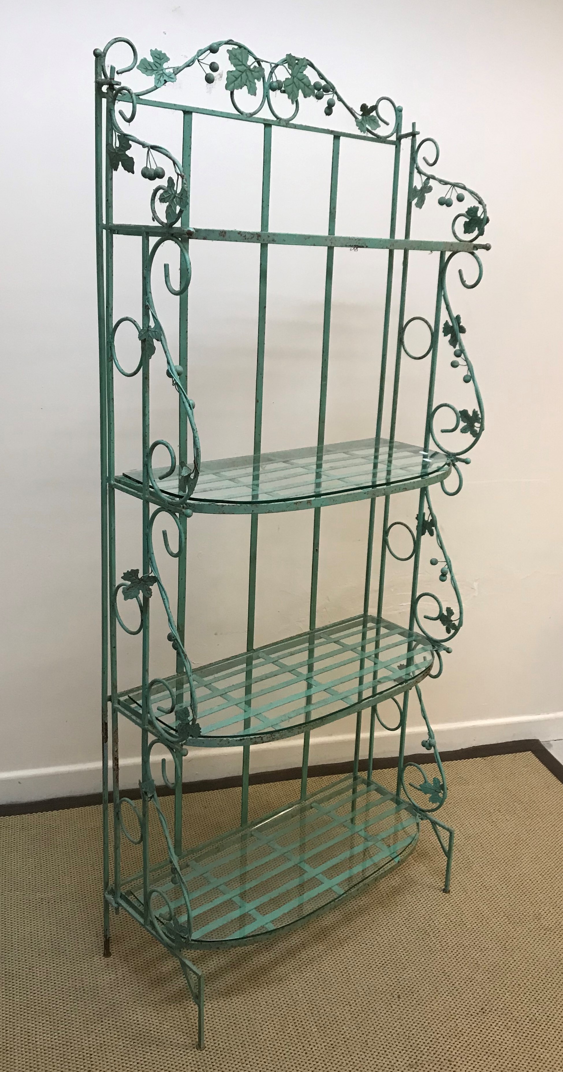 A modern green painted wrought iron shelf unit with grape and vine decoration, the folding sides