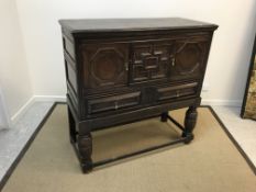 An oak cupboard on stand in the 17th Century manner, the upper section with two panelled cupboard