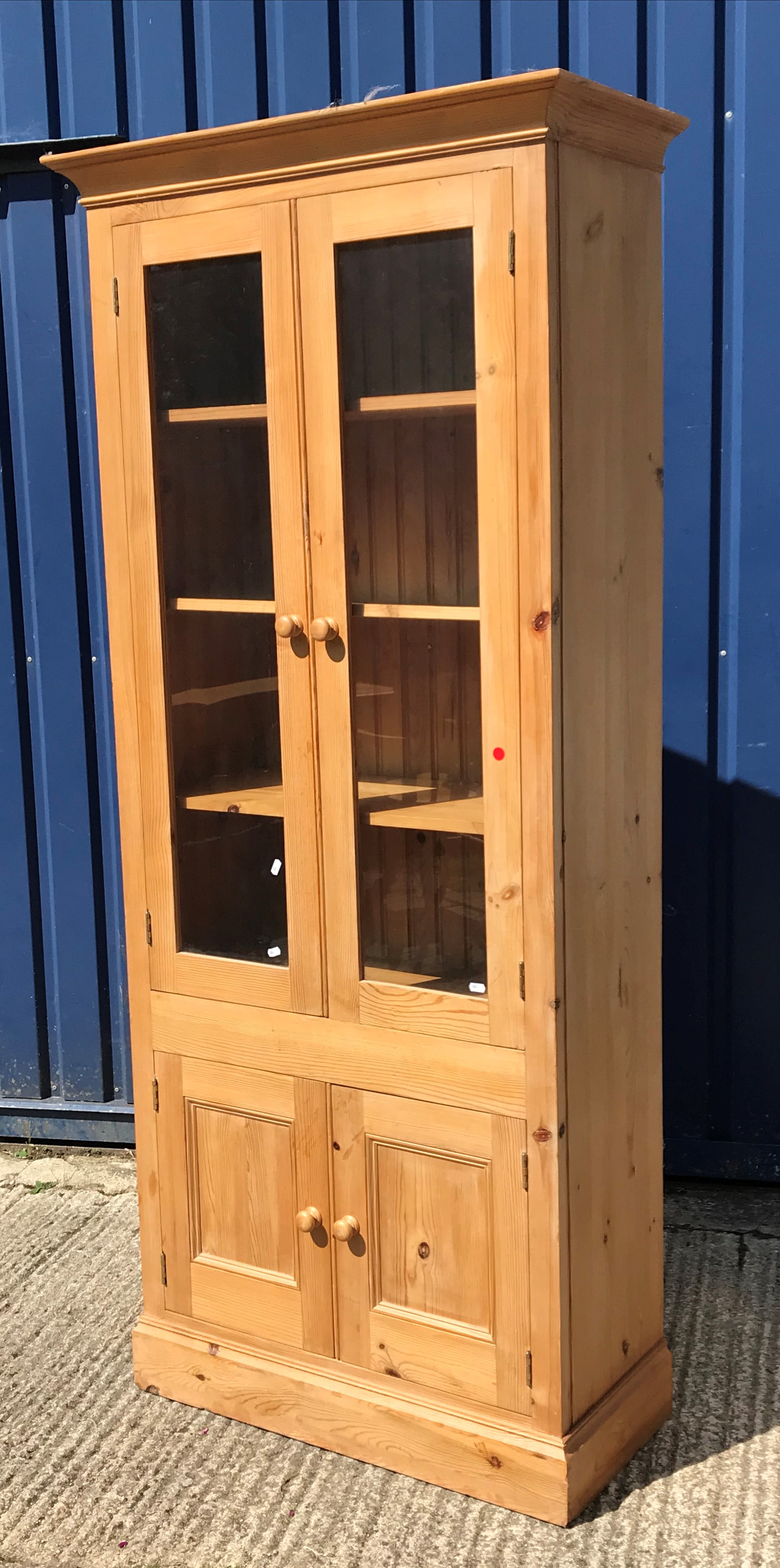 A modern pine display cabinet with moulded cornice over two glazed doors enclosing three shelves