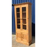 A modern pine display cabinet with moulded cornice over two glazed doors enclosing three shelves