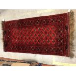 A Bokhara rug, the central panel set with repeating medallions on a dark red ground within stepped