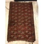 A Bokhara rug, the central panel set with repeating rows of medallions on a red ground within a