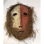 An African tribal mask with red and white painted decoration and grass hair 35 cm long