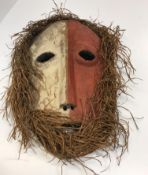 An African tribal mask with red and white painted decoration and grass hair 35 cm long
