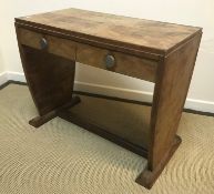 A 1930s Art Deco walnut two drawer writing table with chrome knob handles raised on tapering plank