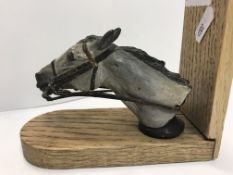 A painted horse head car mascot housed on an oak base as book end, the mascot itself approx 7.5cm