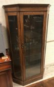 A mid 20th Century oak single door display cabinet with glazed canted side panels raised on a plinth