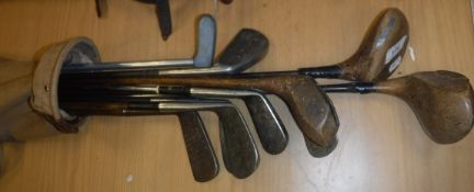 A leather trimmed canvas golf bag and contents of ten hickory shafted and other clubs including AM