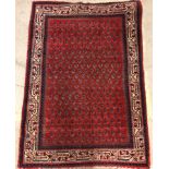 A Persian rug, the central panel set with repeating stylised hook motifs on a red ground,