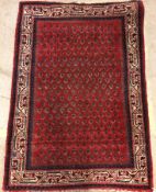 A Persian rug, the central panel set with repeating stylised hook motifs on a red ground,