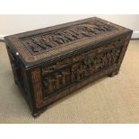 An Eastern ebonised and carved camphor wood trunk with all over figural panel decoration within